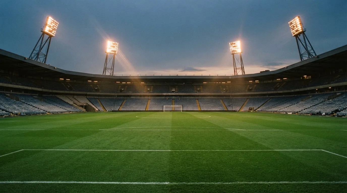 Een leeg voetbalstadion met lichtmasten bij schemering