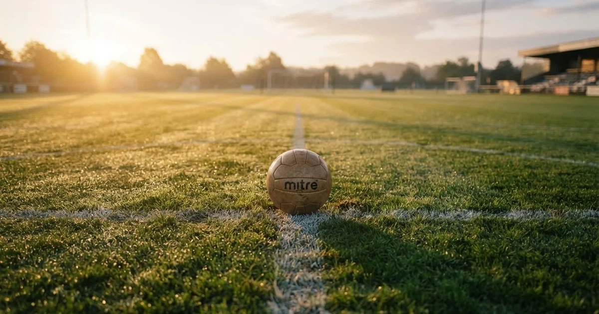 Een voetbal op de middenstip van een grasveld in het ochtendlicht