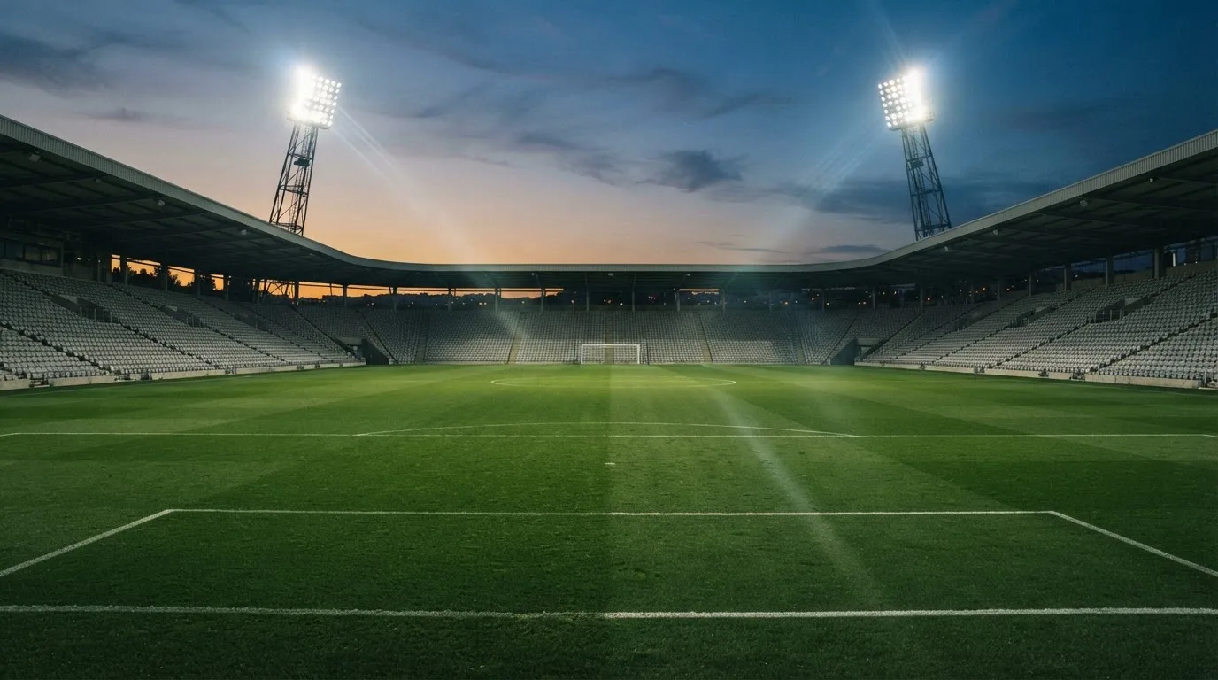 Een leeg voetbalstadion met lichtmasten bij schemering