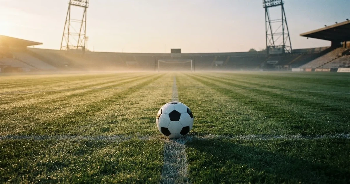 Een voetbal op de middenstip van een grasveld in het ochtendlicht