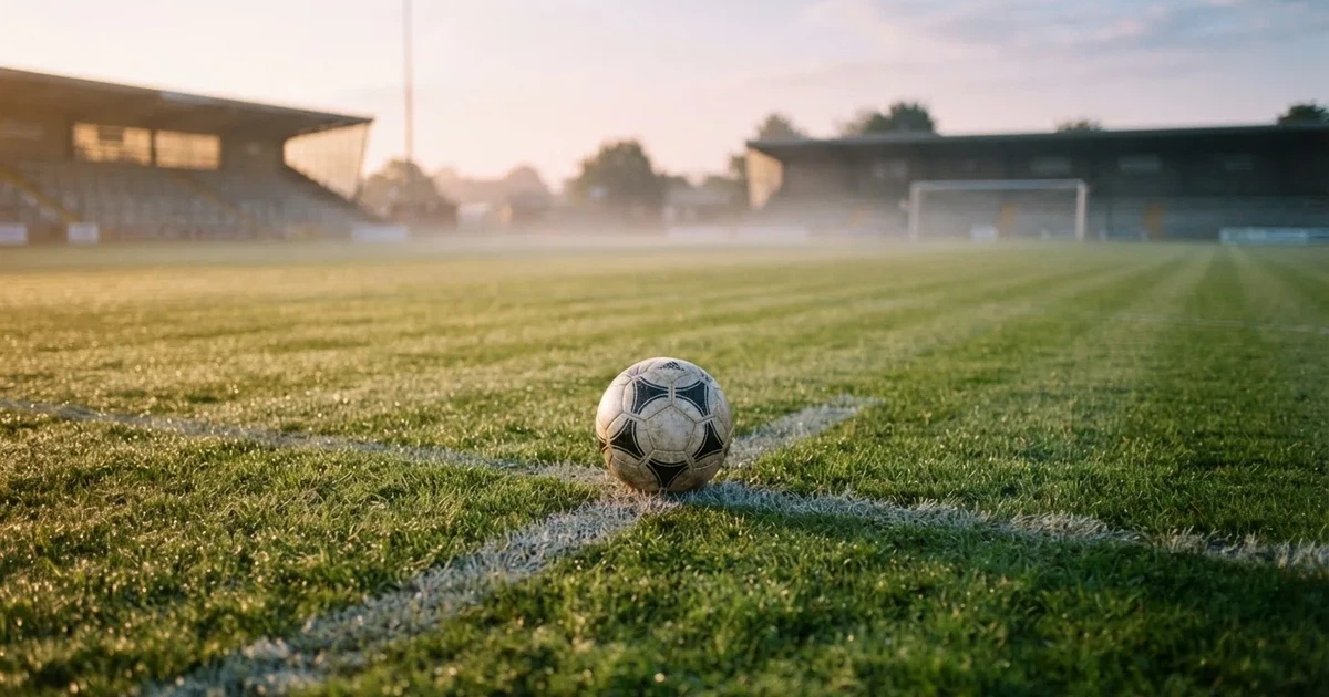 Een voetbal op de middenstip van een grasveld in het ochtendlicht