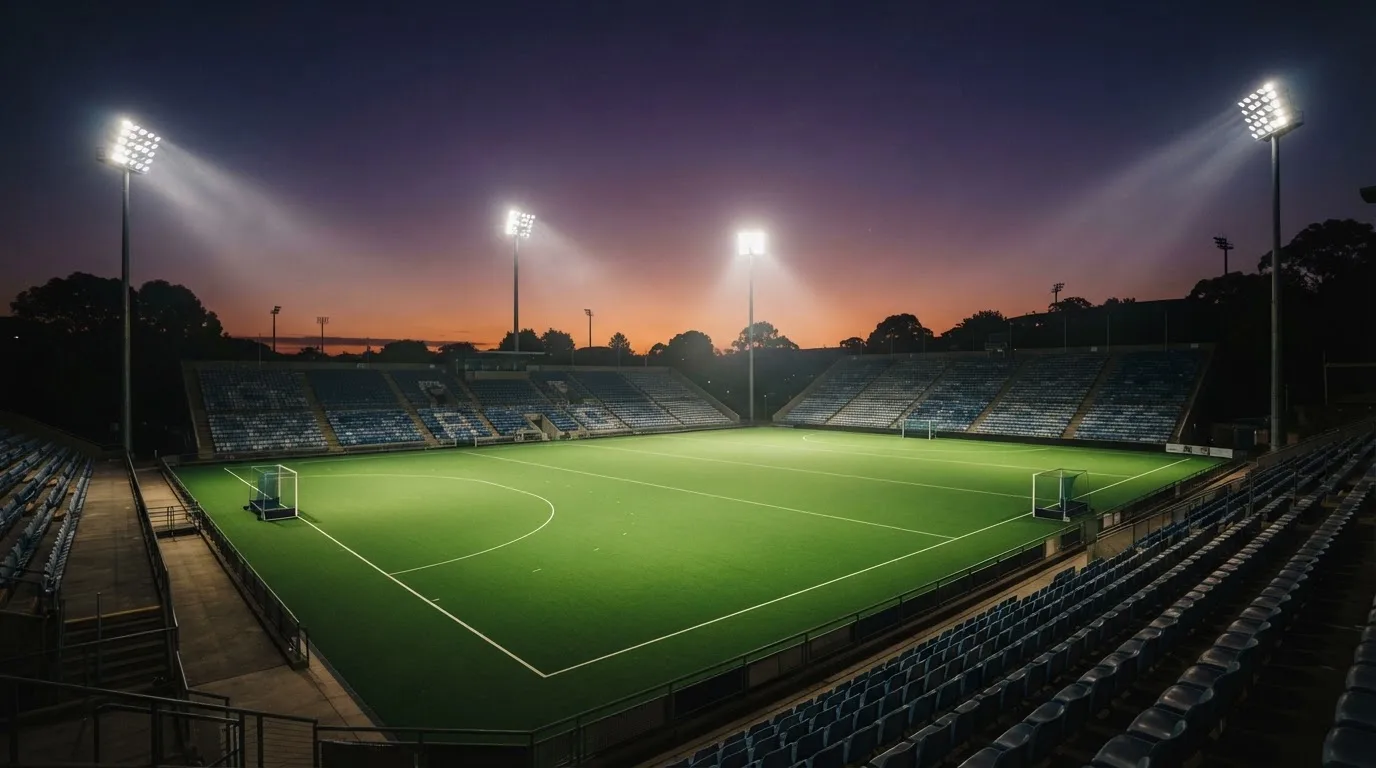 Een leeg voetbalstadion met lichtmasten bij schemering